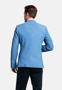 Lichtblauwe, op maat gemaakte blazer met een gladde textuur, een enkele split achter en gebuttonde mouwen. Gestyled met een donkere broek.