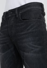 Jeansy z ciemnego denimu o dopasowanym kroju, wyposażone w tradycyjny wzór z pięcioma kieszeniami i metalowe zapięcie na guzik w pasie.