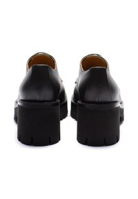 Scarpe in pelle nera con design arrotondato, dotate di un tacco spesso testurizzato e dettagli minimi. Interno foderato in beige.