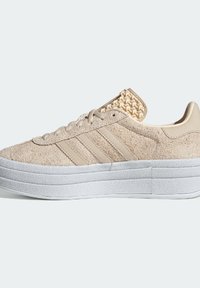 Beige suede sneaker with a white platform sole, featuring three horizontal stripes and a woven accent on the heel.