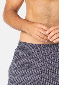 Shorts de bain bleu marine avec un motif blanc répété, dotés d'une taille élastique et d'une coupe décontractée. Tissu doux avec une texture lisse.