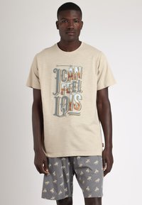 Camiseta beige con un diseño gráfico de texto multicolor, combinada con pantalones cortos grises que presentan un patrón repetido de caballos de color marrón claro.