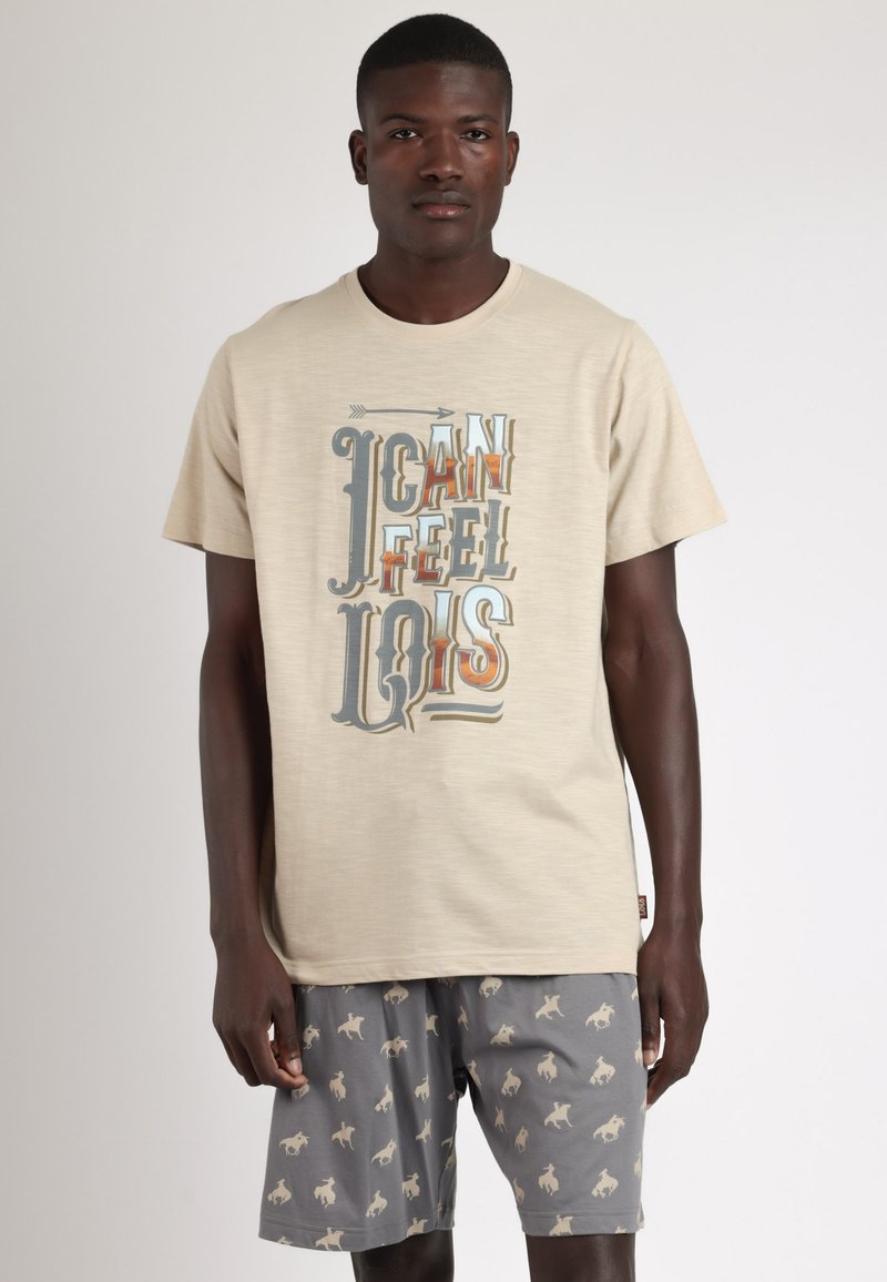 Camiseta beige con un diseño gráfico de texto multicolor, combinada con pantalones cortos grises que presentan un patrón repetido de caballos de color marrón claro.