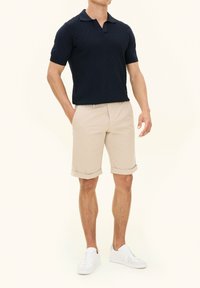 Marinblå kortärmad polo med diamanttextur, kombinerad med beige upprullade shorts och vita sneakers. Enkelt, modernt design.