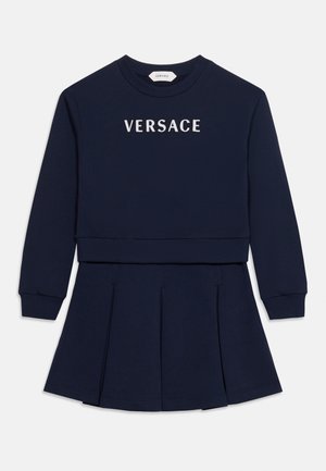 Rochie bleumarin cu mâneci lungi, fustă plisată și logo alb VERSACE pe piept.