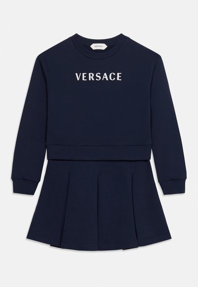 Robe bleu marine à manches longues avec jupe plissée et logo VERSACE blanc sur la poitrine.