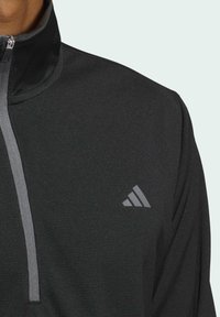 Haut de sport noir à zip quart avec un col gris et un logo subtil. Présente une texture lisse et un design ajusté pour le confort et la performance.