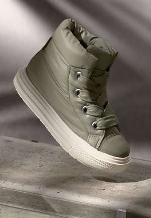Oliven grønn polstret høyhælte sneakers med grå detaljer, rund tå, flat hvit såle og metallhull, med lisser i matchende farge.