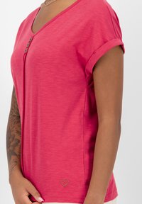 Roze T-shirt met korte mouwen en V-hals, gemaakt van een zachte, gestructureerde stof. Voorzien van drie decoratieve knopen en een klein hartlogo aan de onderkant aan de voorkant.