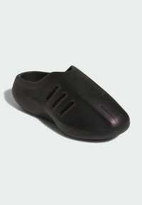 Svart slip-on sko med slät stängd tå, tre ventilationsslitsar på sidan och tjock sula, visad mot en enfärgad ljus bakgrund.