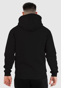Sudadera con capucha negra de textura suave, que cuenta con un bolsillo tipo canguro y puños y dobladillo de canalé. La vista trasera muestra el detalle de la capucha.