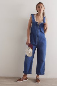 Plave traper hlače s prednjim patentnim zatvaračem i širokim nogavicama. Uz to je bijela čipkasta potkošulja i smeđe cipele s vezicama. Drži bijelu kapu.