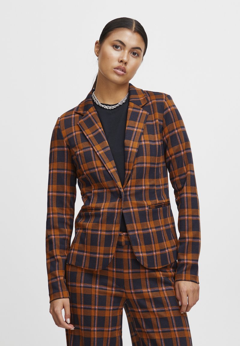 Rutet blazer i orange og navy med en tætsiddende design, enkeltknaplukning og klaplapper. Bukserne har et matchende mønster.