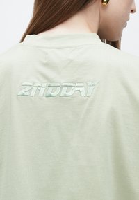 Lichtgroen T-shirt met een losse pasvorm, met een geaderd geborduurd logo "2NDDAY" op de achterkant in een iets donkerdere tint.