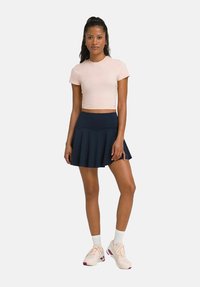 Lichtroze cropped t-shirt gecombineerd met een marineblauwe uitlopende rok. Model draagt lichte sneakers met witte sokken. Glad materiaal, casual ontwerp.