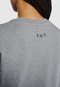 Grijze katoenen T-shirt met korte mouwen, met een gestikt zwart "F.U.T."-label op de achterkant van de halslijn. Zachte textuur, casual ontwerp.