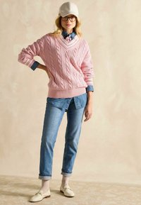 Heled roosa soonik, millel on V-kaelus, koos denimsärgi, siniste teksade ja kreemjate lohakatega, millel on kuldsed detailid. Igapäevane riietus.