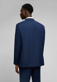 Giacca di abito blu navy con una texture liscia, apertura singola sul retro e polsini abbottonati. Design semplice senza motivi o accenti visibili.