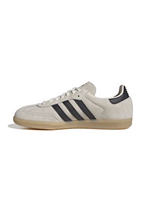 Niskoprofilowy beżowy zamszowy sneaker z czarnymi paskami, gumową podeszwą i sznurowaniem widziany z boku na białym tle.