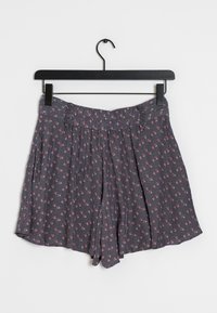 Pantaloni corti grigi a fiori con piccoli fiori rosa e bianchi, design plissettato, cintura elasticizzata, appesi a un semplice appendiabiti nero.