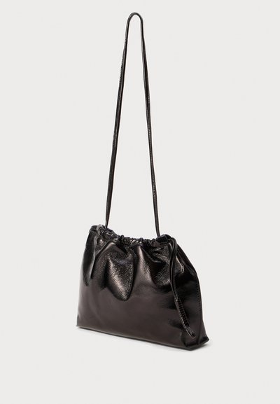 Borsa a spalla in pelle nera con parte superiore arricciata e lunga tracolla sottile, texture leggermente lucida, esposta su uno sfondo chiaro e semplice.