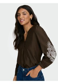 Brun langærmet bluse med V-hals, med knapdetaljer og hvid blomsterbroderi på ærmerne. Blødt, struktureret materiale.