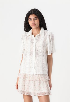 White short-sleeve shirt with lace detailing and button closure, paired with a layered sheer skirt featuring a floral pattern.
