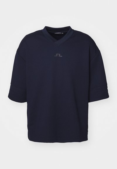 Tummansininen lyhythihainen polo-paita, jossa on V-pääntie ja teksturoitu kangas. Rinnassa on hienovarainen logoyksityiskohta.