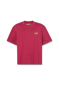 Camiseta de manga corta color marrón, hecha de algodón, con una etiqueta cuadrada en el pecho que presenta texto multicolor y un diseño de logo.