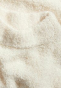 Fuzzy krämfärgad tyg med en mjuk, texturerad yta. Subtila färgvariationer och en rundad halslinje är synliga.