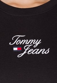 Camiseta de algodón negra con el texto bordado en blanco "Tommy Jeans" y un pequeño logotipo en rojo, blanco y azul debajo.
