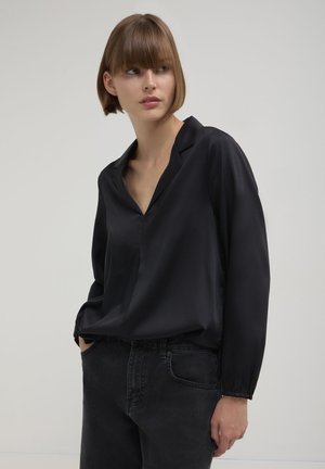 Blusa in satin nera con scollo a V, maniche lunghe e polsini con bottoni. Texture liscia e vestibilità comoda. Abbinata a jeans scuri.