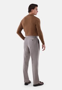 Brauner Strickpullover, hellgraue, maßgeschneiderte Hose mit flacher Vorderseite und Gesäßtasche, kombiniert mit dunklen Loafers, von hinten betrachtet.