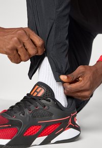 Black athletic pants with zippers at the ankles, paired with red and black athletic shoes, featuring mesh accents and white socks.