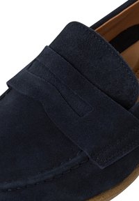 Mörkblå mocka slip-on sko med rund tå och ett dekorativt band över framsidan. Har en texturerad yta och en kontrasterande sula.