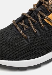 Baskets de sport noires avec une tige en mesh texturé, lacets speckled orange et une semelle intermédiaire blanche. Comprend une semelle extérieure en caoutchouc noir et des œillets.