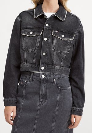 Black cropped denim jacket with silver button closures and jewel embellishments on collar and chest pockets worn over matching denim skirt.