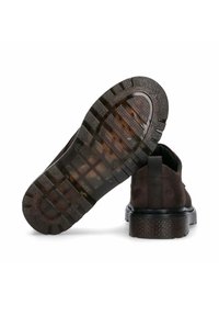 Bruine suède schoenen met een stevige zwarte rubberen zool. De zool heeft een gestructureerd, gepatterned profiel voor grip.