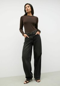 Bruine langslavige top gecombineerd met hoge taille, wijde zwarte denim jeans. De outfit heeft zakken en elegante zwarte hakken.