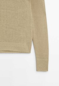 Beige neulepaita, jossa on tekstuurinen pinta, ribbauskurtseja ja helmaa sekä renon malli, joka korostaa ompelukuviota.