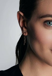 Złote kolczyki w kształcie kół z delikatnym łańcuszkiem zwisającym z dołu, o gładkim wykończeniu i błyszczącej fakturze.