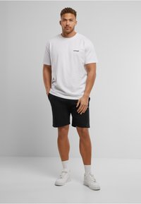 White cotton t-shirt with "UPGRADE" print, black shorts, white sneakers, and white ankle socks. Simple, casual outfit with no patterns.