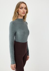 Długi rękaw bluzki z dzianiny w kolorze szaro-heather z wysokim kołnierzem, w połączeniu z legginsami w ciemnym brązie o wysokim stanie. Gładka tekstura, dopasowany krój.
