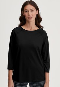 Zwarte, langmouwen top met een ronde halslijn en raglanmouwen, gemaakt van een zachte stof. Gecombineerd met zwarte en witte polkadot leggings eronder.