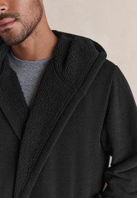 Robă cu glugă neagră, cu un guler texturat căptușit cu fleece și material cu dungi. Designul include un guler stil șal și o croială lejeră.
