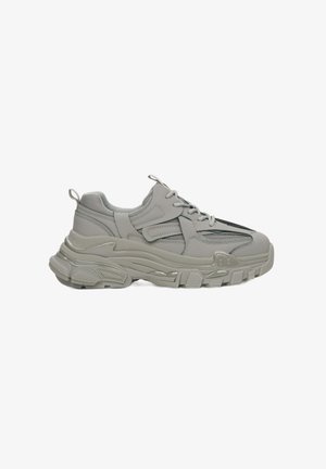 Light grey sneakers with a chunky sole, featuring layered mesh and synthetic material, and decorative black accents along the upper.