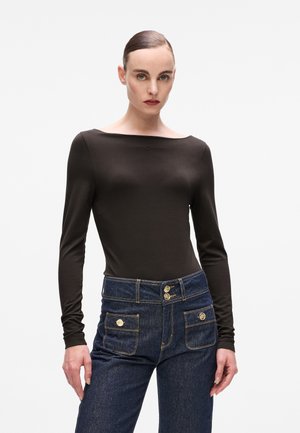 Long-sleeve dark brown top with a wide neckline, paired with high-waisted dark blue denim jeans featuring gold hardware and decorative pockets.