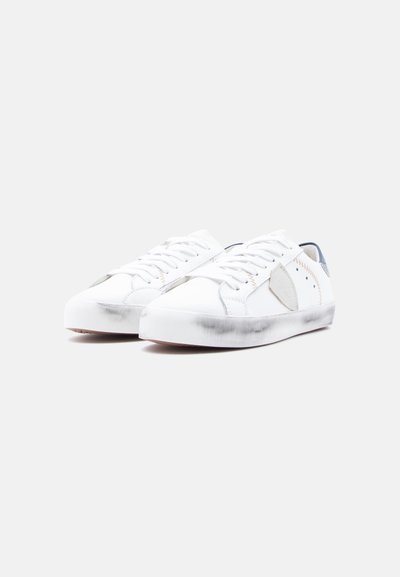 Λευκά αθλητικά παπούτσια χαμηλού προφίλ με ομαλή υφή, με γκρι λεπτομέρειες, αντίθετη ραφή και ελαφρώς φθαρμένη λαστιχένια σόλα.