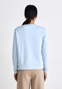 Világoskék pulóver kerek nyakkal, bordás mandzsettákkal és szegéllyel. Puha, sima textúrájú, varrat nélküli dizájn, bézs nadrággal párosítva.