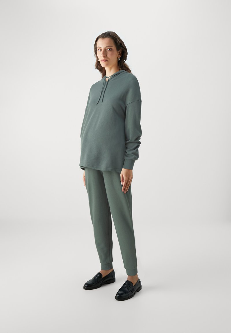 Green sweatshirt and joggers set in a soft fabric, featuring a hood and drawstring, paired with black shoes. Simple, relaxed fit design.